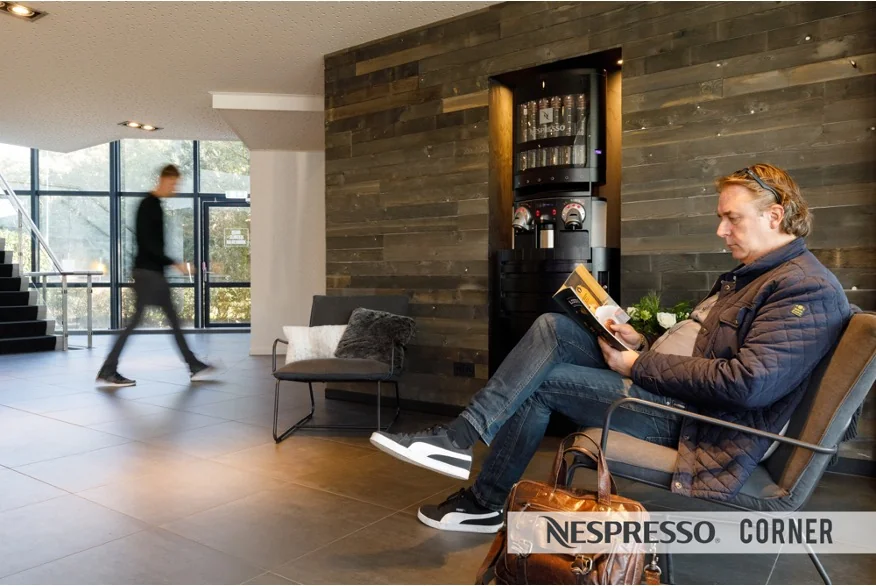 Man leest een boek in een wachtruimte met een Nespresso-hoek aan de Baarnsche Dijk.